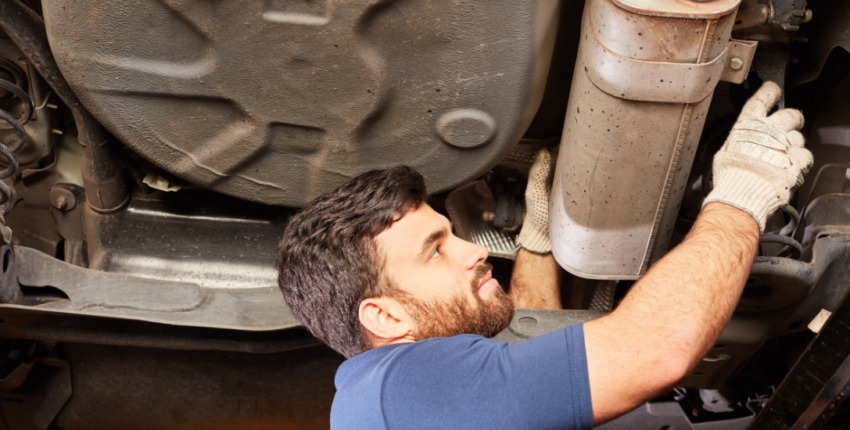 Technician performing emission system check under a vehicle.
