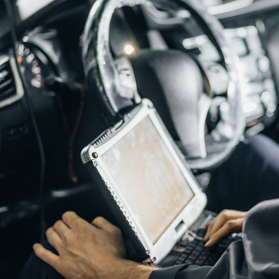 Technician using diagnostic scanner in vehicle for computer diagnostics.