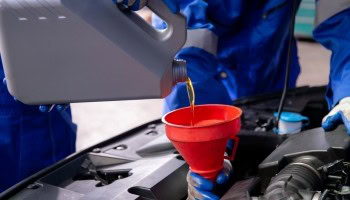 Technician pouring oil into car engine during maintenance.
