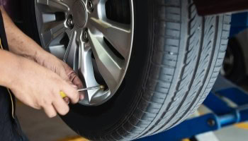 Technician inspecting car tire at Cliffs Edge Automotive workshop.