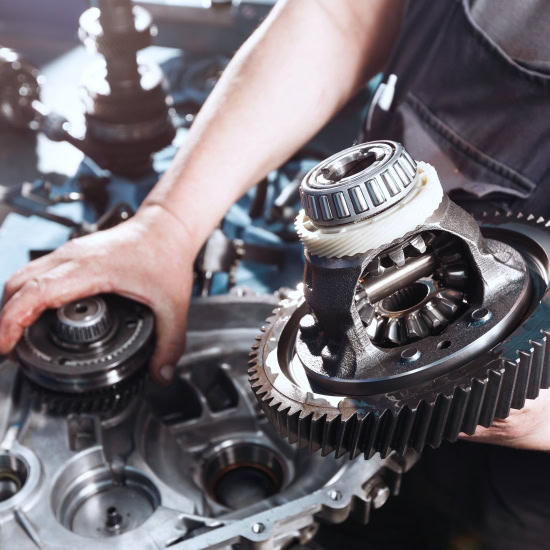 Technician repairing vehicle transmission with gears and tools.