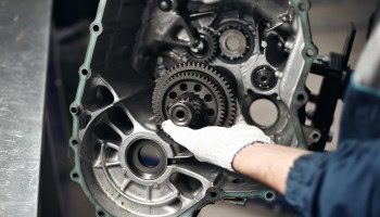 Technician repairing car transmission with gears and tools.