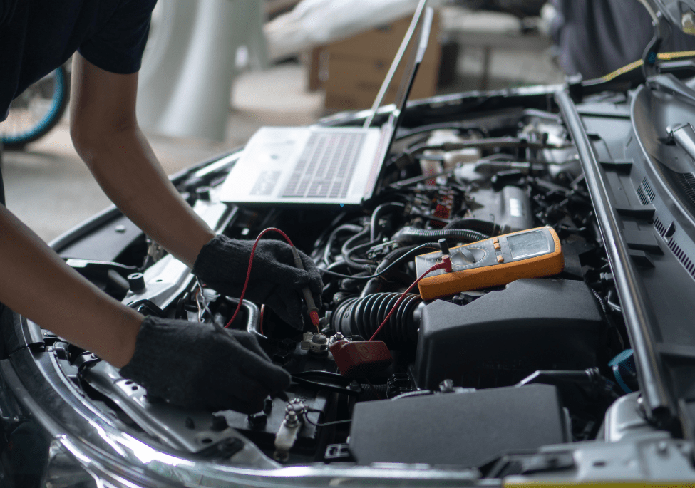 Technician inspecting car engine with diagnostic tools and laptop.