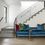 Vibrant blue velvet sofa with multicolored throw pillows in a modern living room with wooden floors.