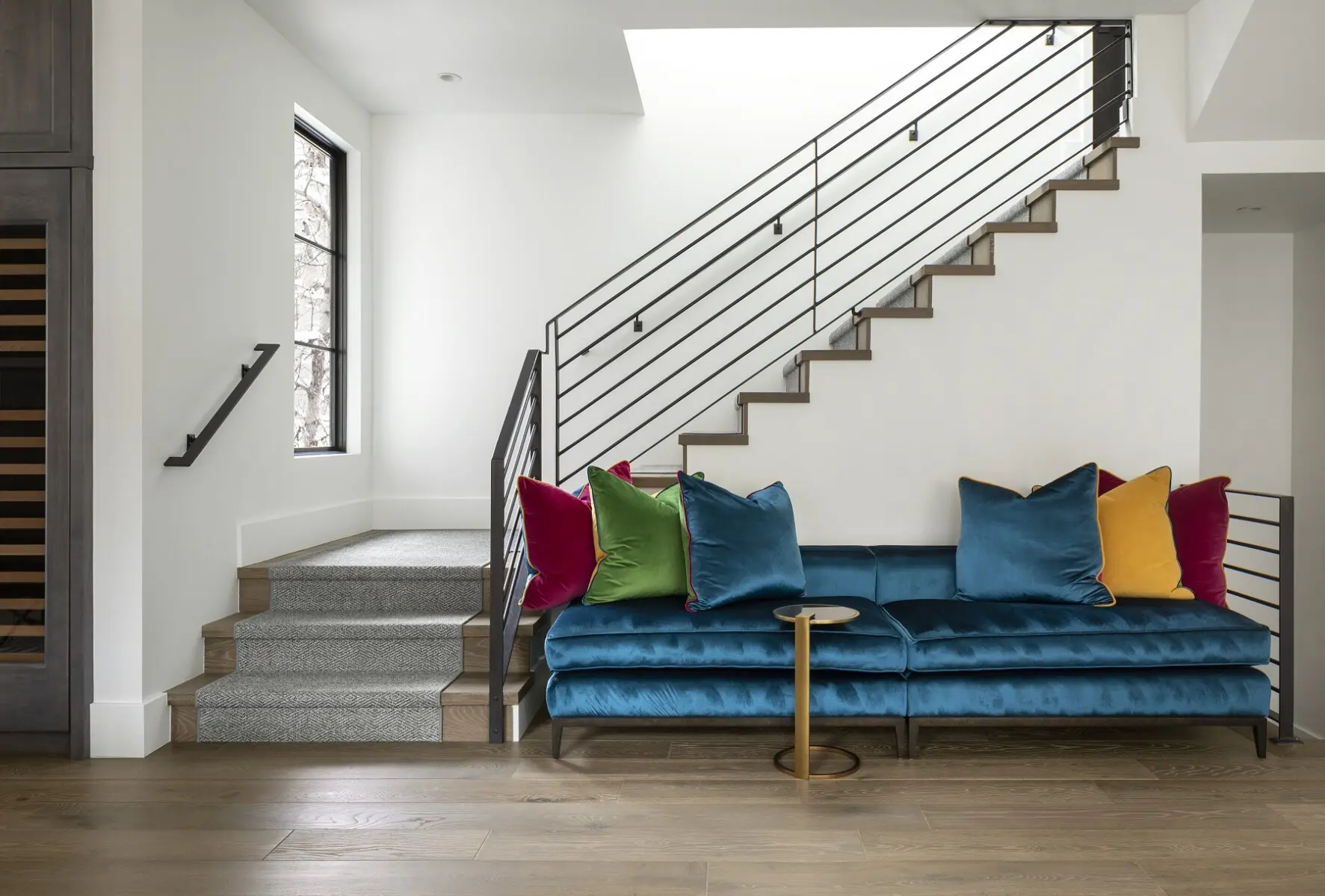 Vibrant blue velvet sofa with multicolored throw pillows in a modern living room with wooden floors.
