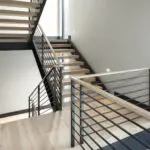 Smooth light wood flooring with black metal staircase and railings in modern interior.