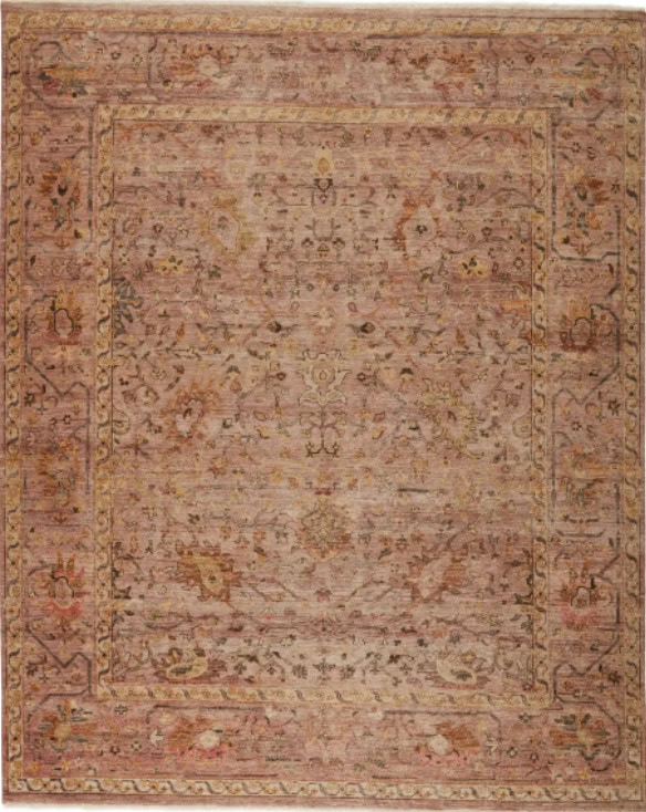 Worn vintage rug with intricate floral and geometric patterns in muted pink and beige tones.