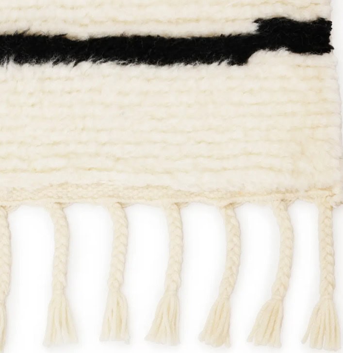 Soft cream wool rug with black stripe and fringe, perfect for cozy and stylish home decor.