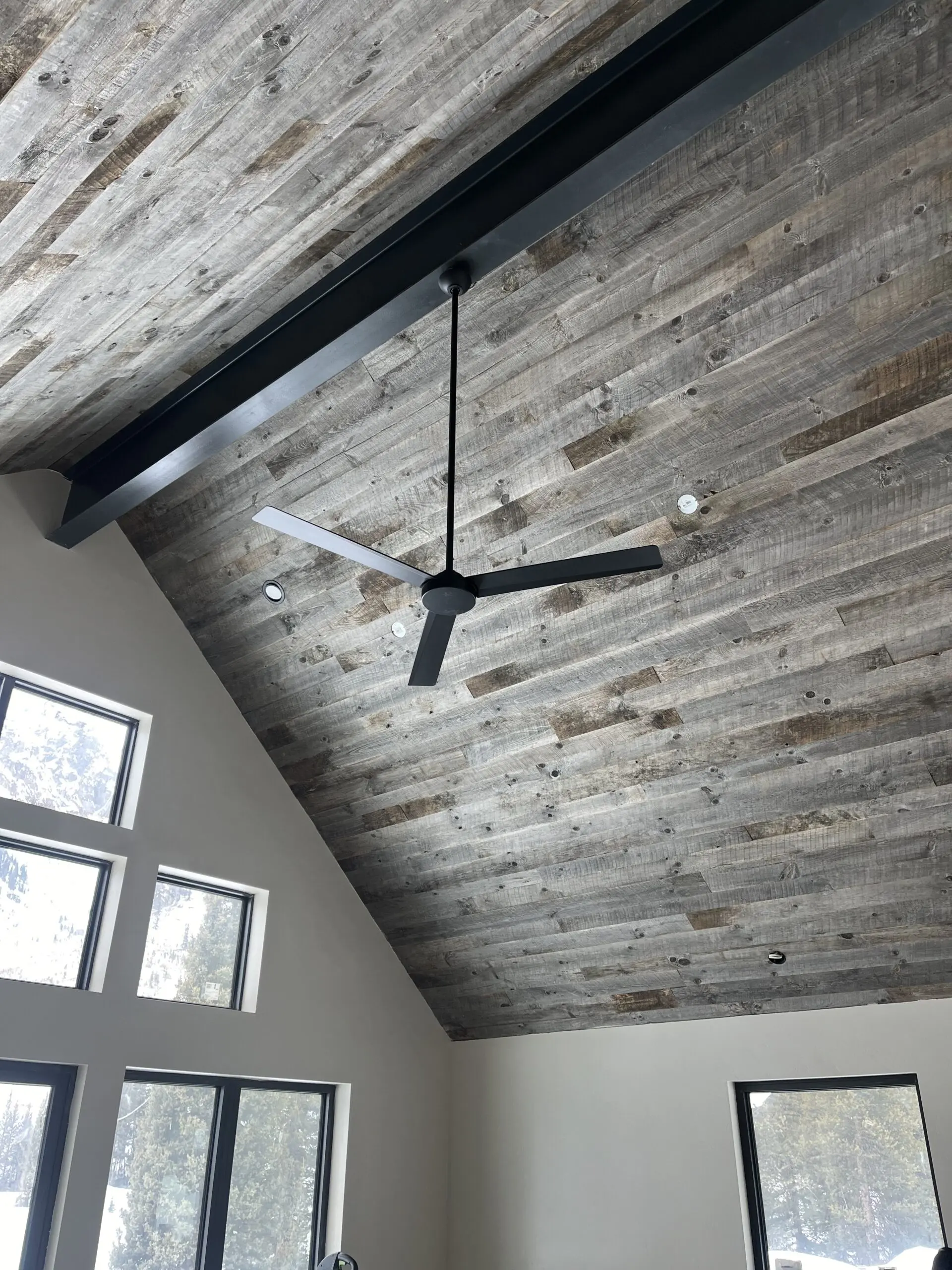 Rustic wood ceiling with black modern fan and large windows, stylish interior flooring and ceiling design.