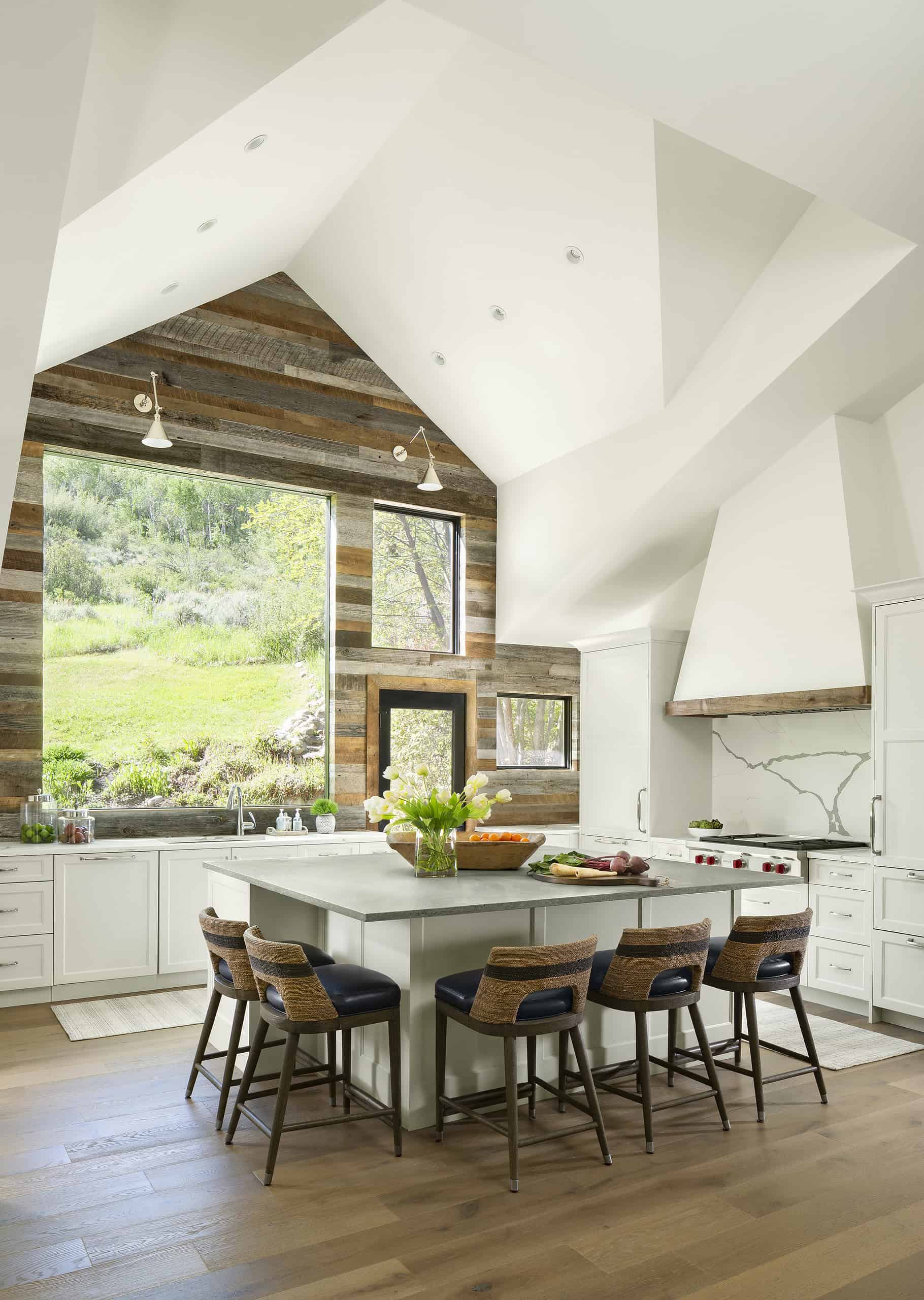 Bright modern kitchen with white cabinets, wooden floors, and large windows overlooking greenery.