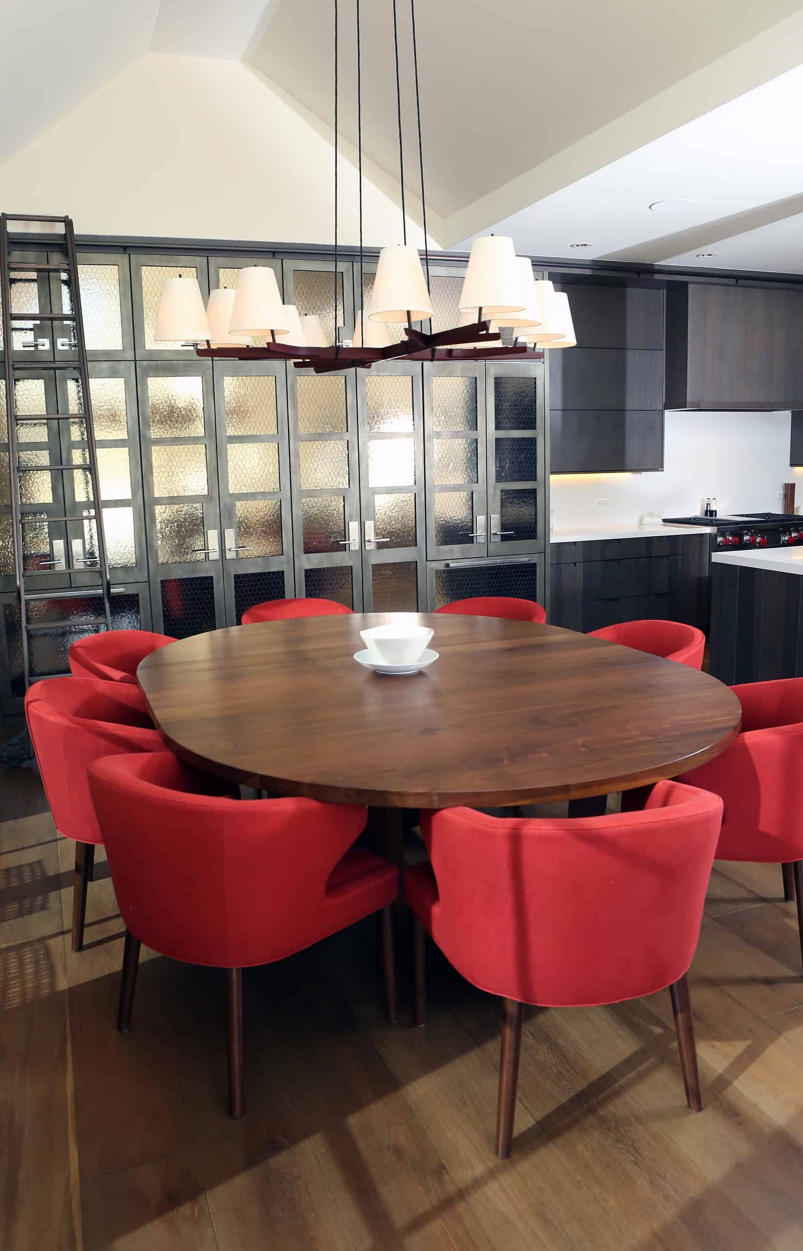 Modern dining room with stylish wooden table and vibrant red chairs, featuring contemporary lighting and sleek cabinetry.