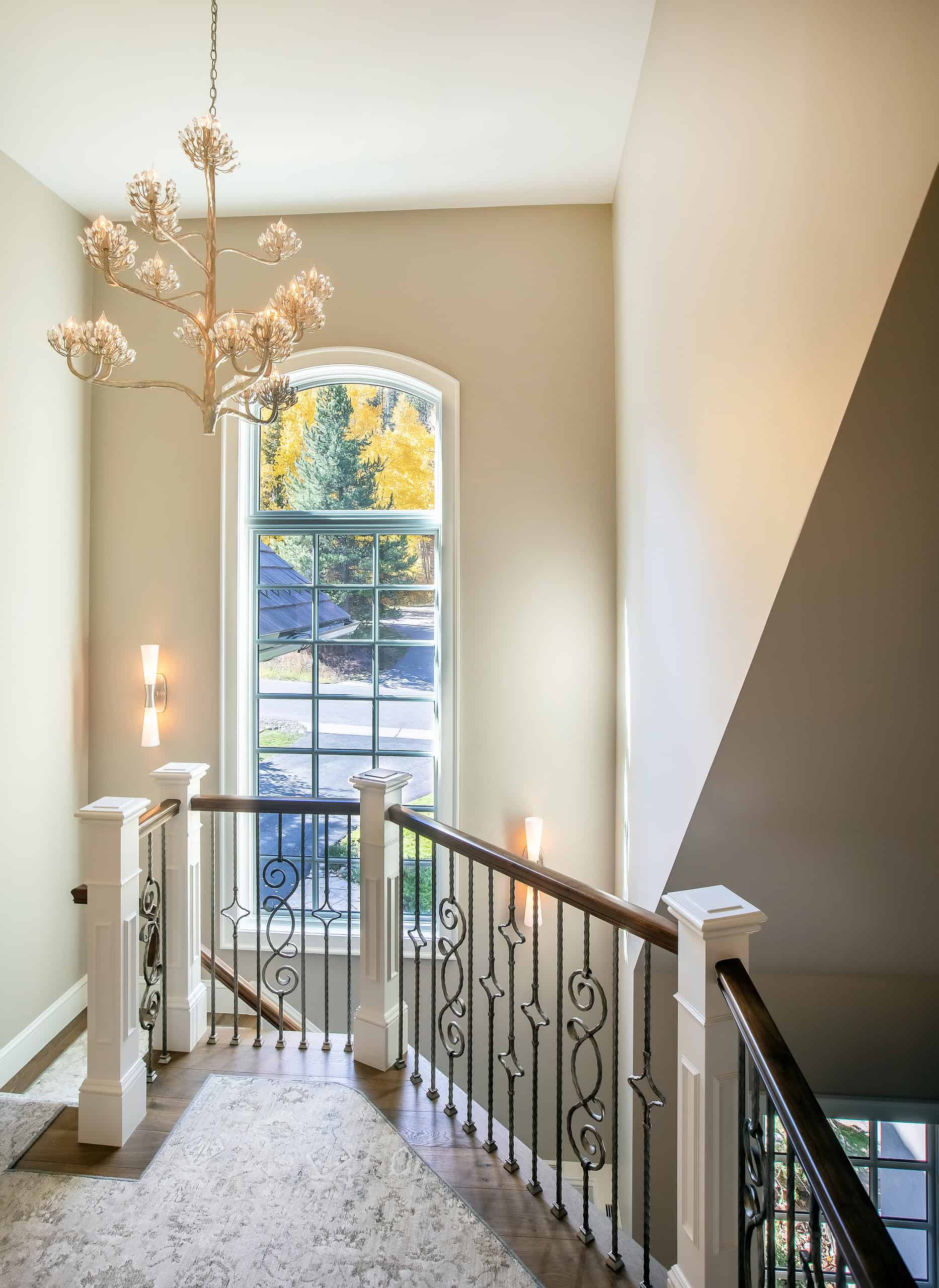 Elegant staircase with wrought iron railing and large arched window in a modern home.