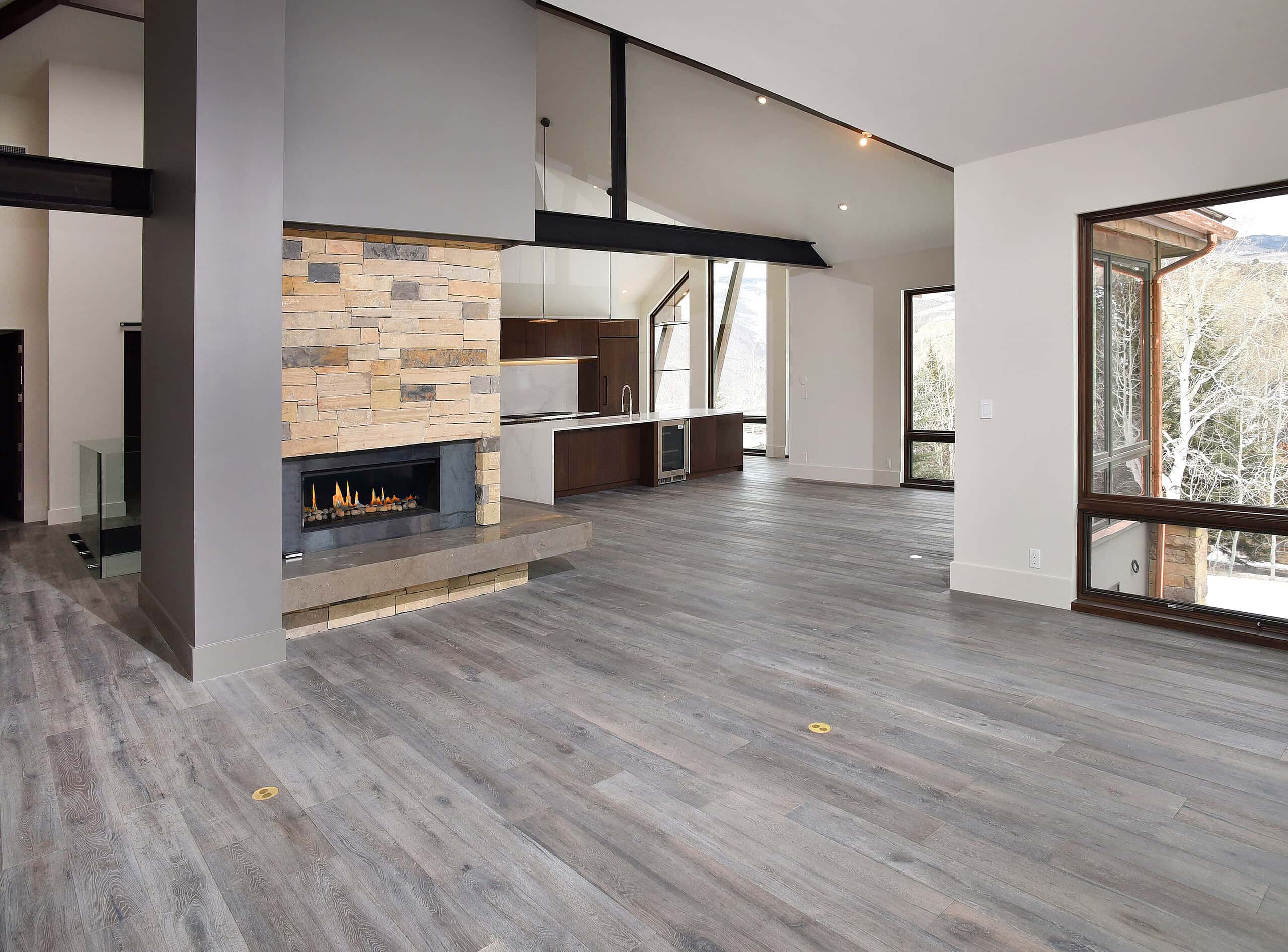 Sleek modern living room with wood flooring, stone fireplace, and large windows showcasing mountain views.