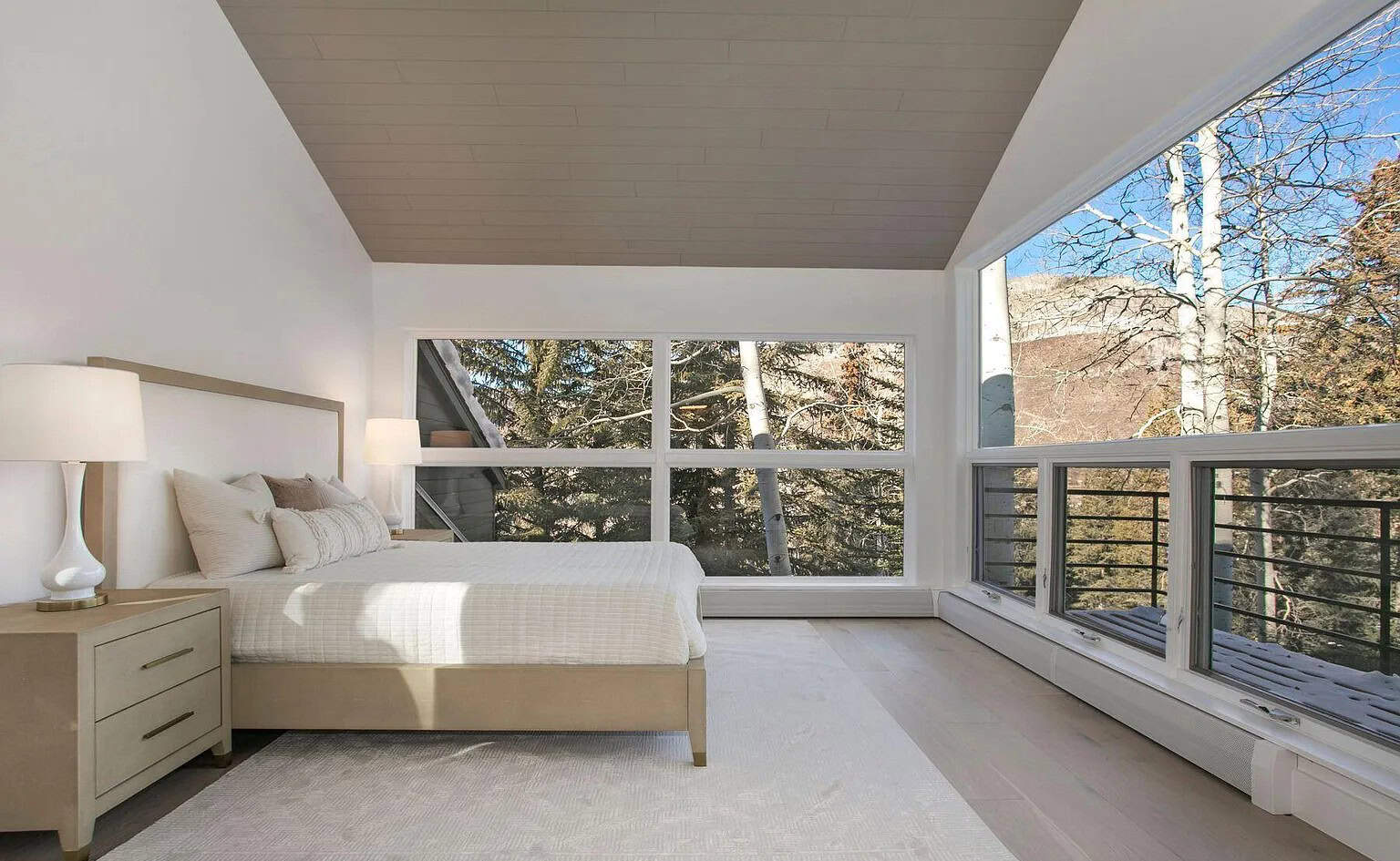 Modern bedroom with large floor-to-ceiling windows showcasing beautiful mountain and forest views.