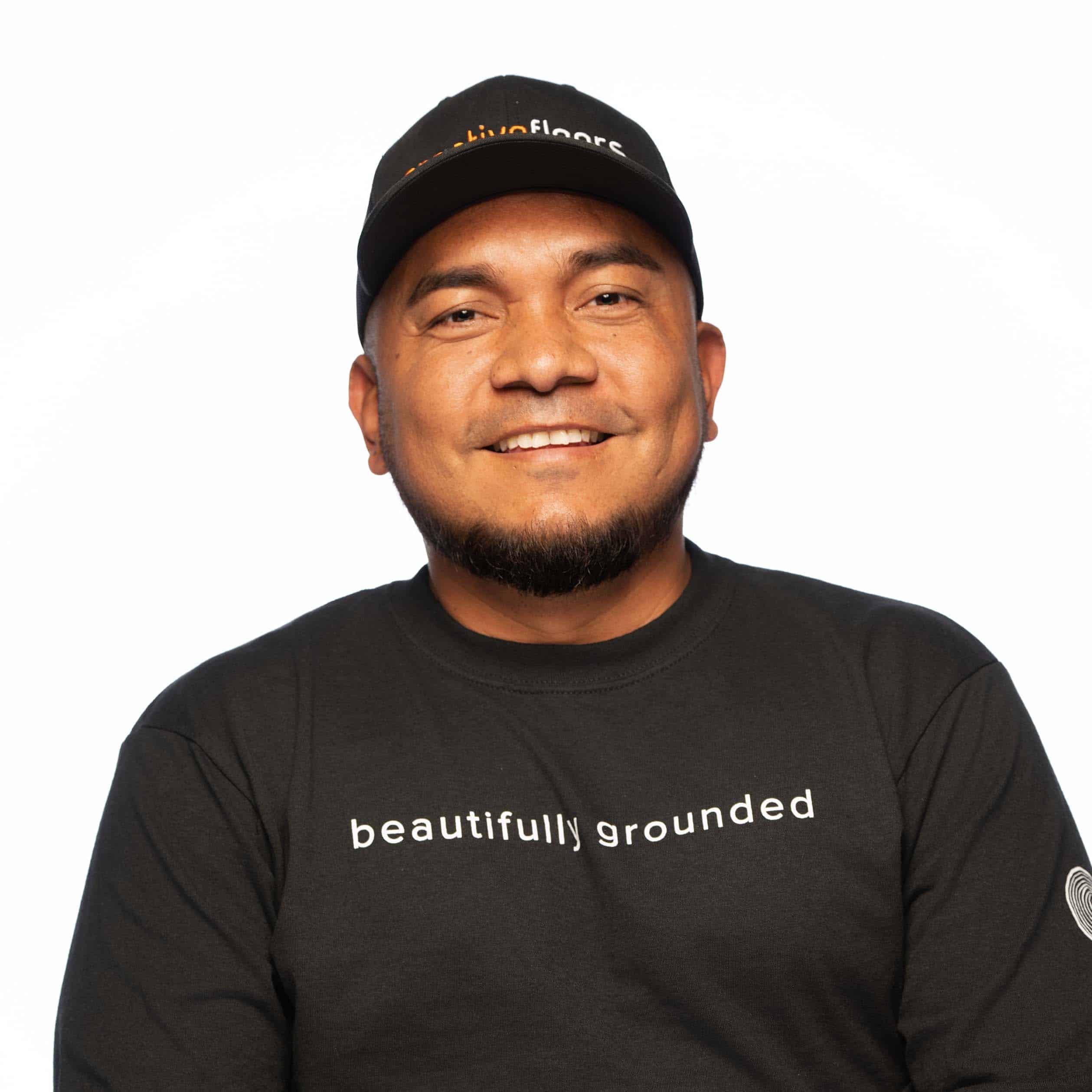 Professional flooring expert wearing branded cap and black t-shirt, smiling confidently, promoting high-quality flooring services.