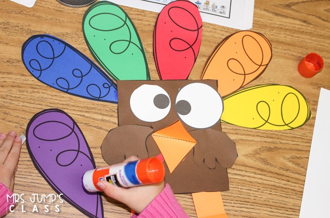A child is putting glue on a purple feather for a turkey craft