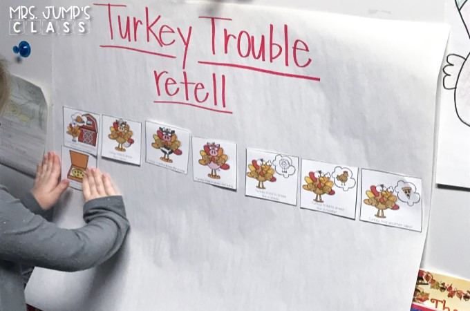 A student is placing a picture card on a large piece of chart paper labeled "Turkey Trouble Retell"