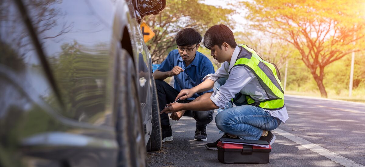 Vehicle repair technicians inspecting a truck tire outdoors.
