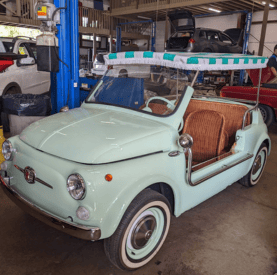 Electric vintage car with retro design and open top, inside a workshop setting.
