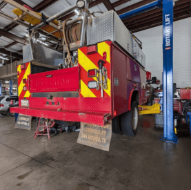 Fire truck service vehicle with safety markings inside an auto repair shop.