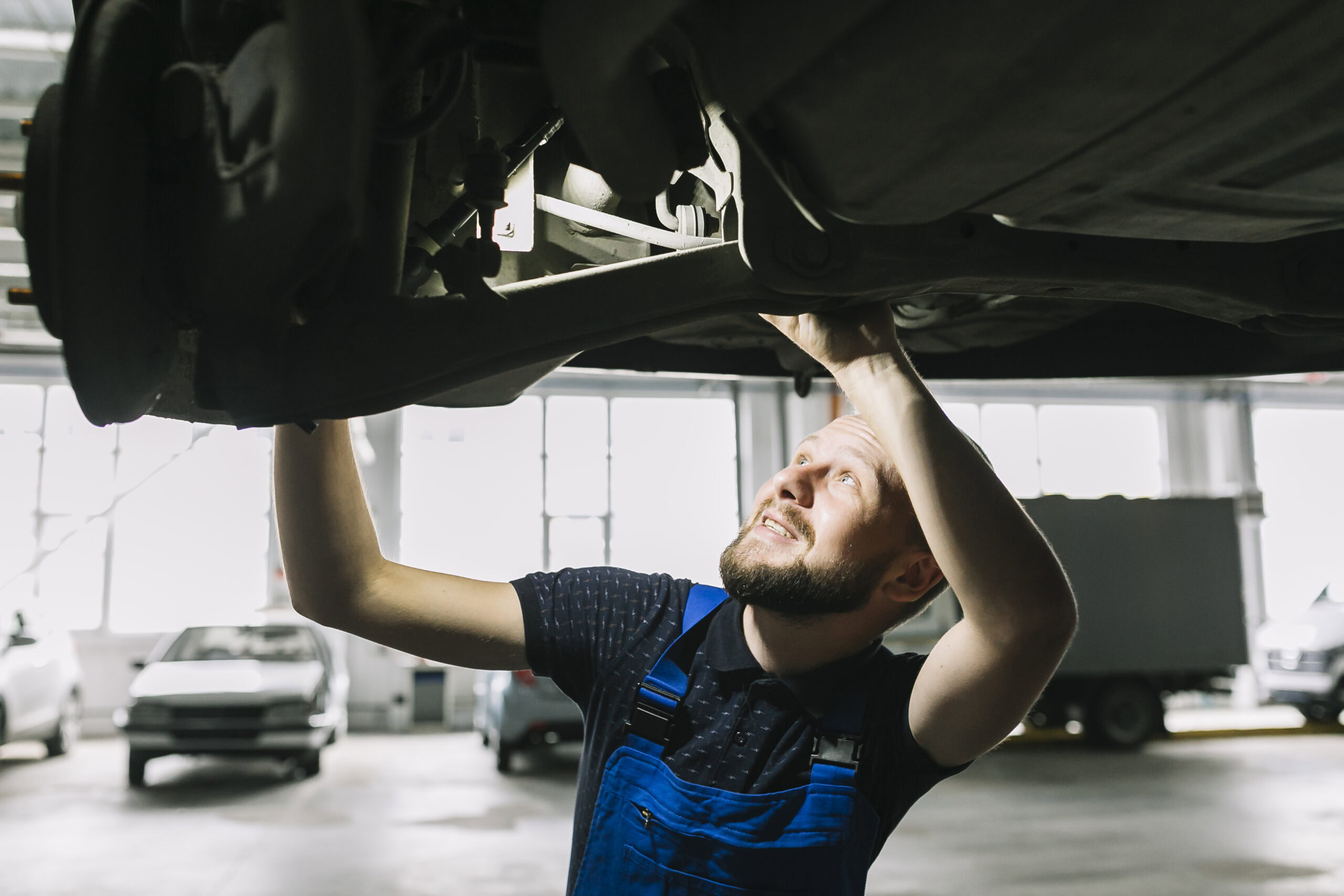 Mechanic inspecting vehicle transmission system in auto repair shop.