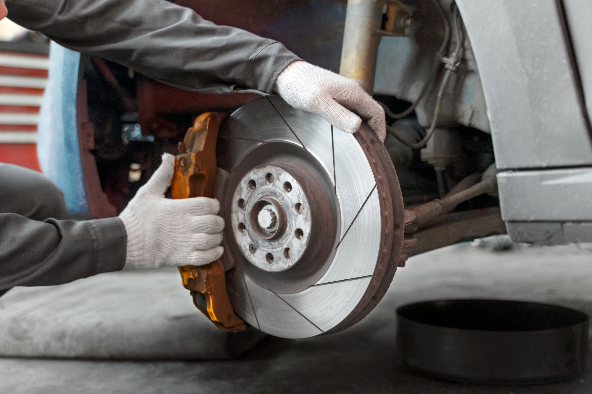 Technician inspecting a vehicle's brake disc and caliper for repair or maintenance.