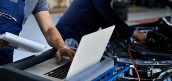 Auto repair technician diagnosing vehicle issues with a laptop.