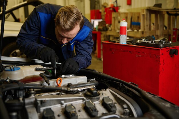 Auto repair technician inspecting car engine in workshop.