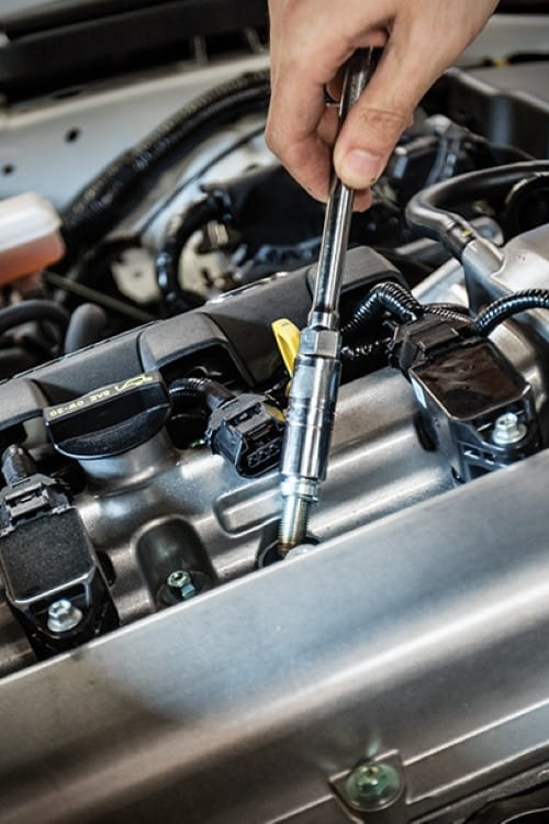 Mechanic inspecting a Japanese vehicle engine with a screwdriver.