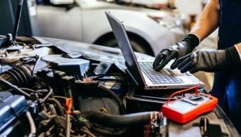 Skilled technician performing diagnostics on a car engine with laptop and tools.