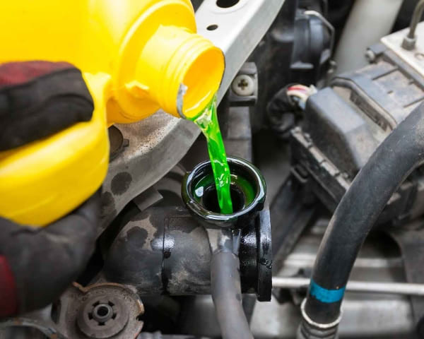 Green coolant being poured into a car's cooling system during maintenance.