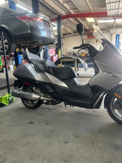 Scooter in auto care shop with car lift and vehicle in background.