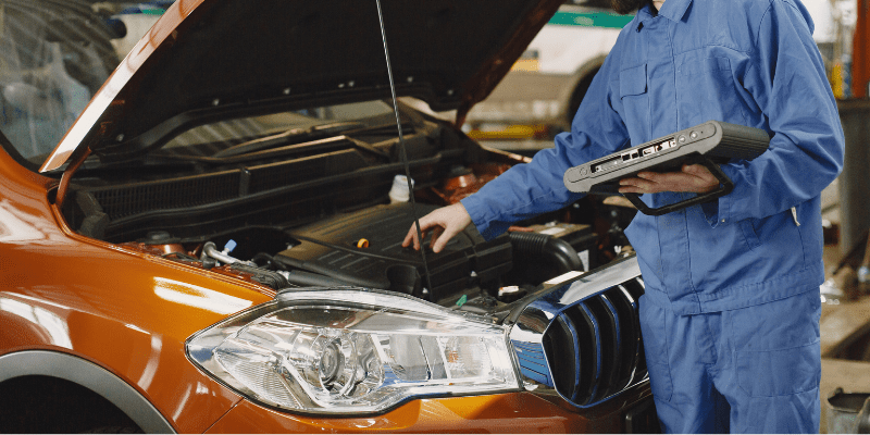 Technician inspecting car engine at Dunn's RevSports repair shop.