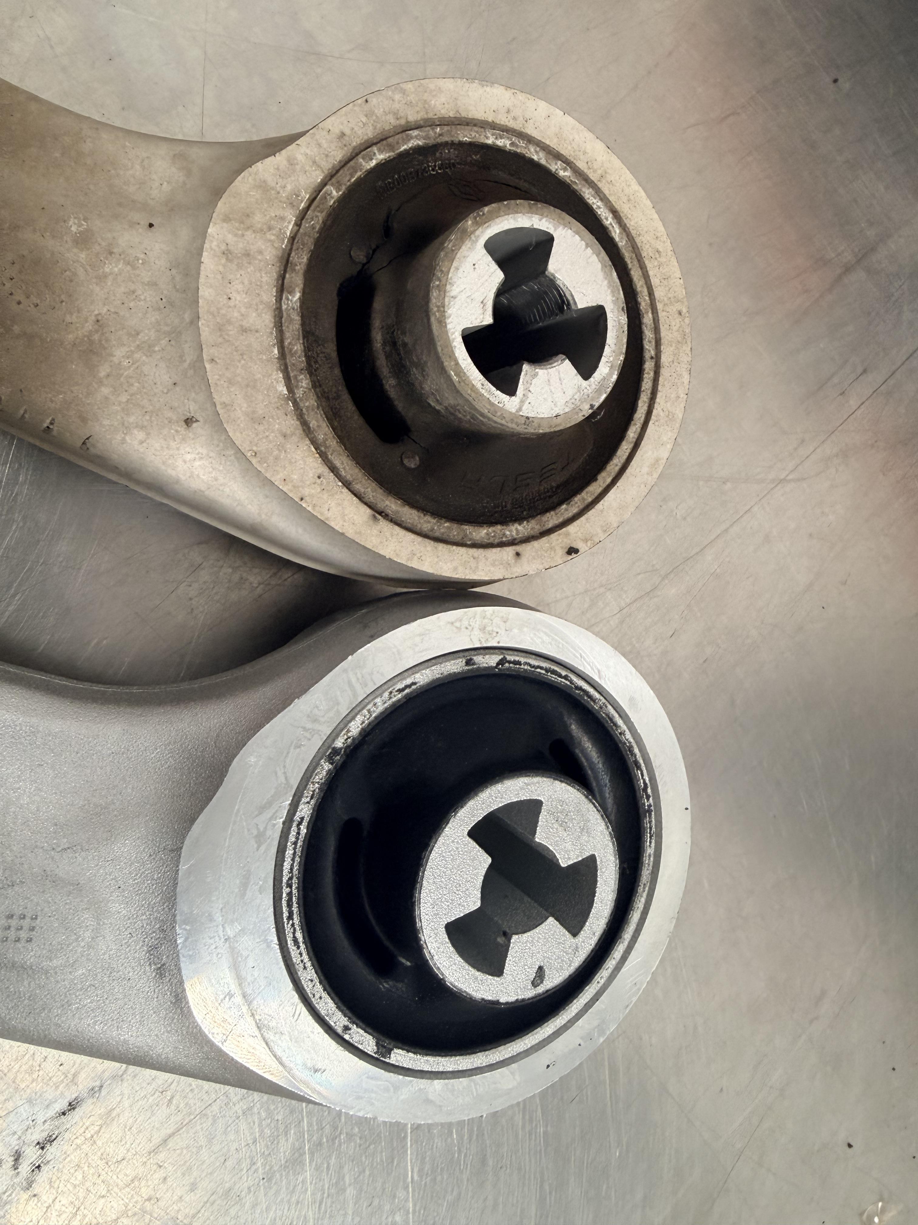 Close-up of worn and new front control arm bushings for Tesla vehicle.