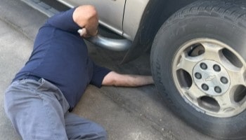 Technician inspecting under vehicle for maintenance or repair needs.