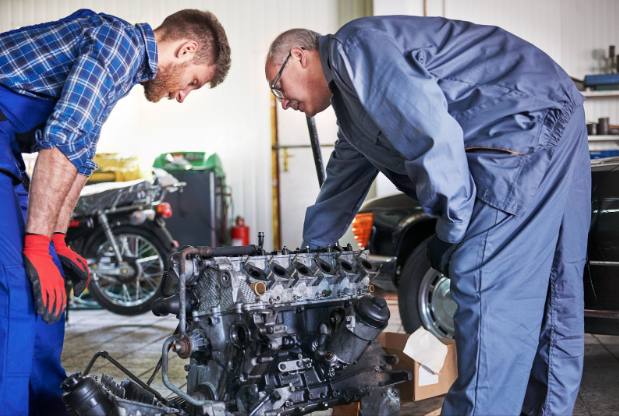Two mechanics inspecting a car engine in a garage during winter.