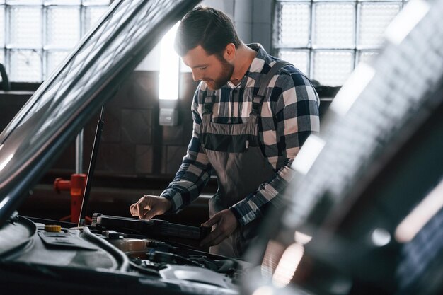 Car mechanic inspecting battery and electrical system in a garage.