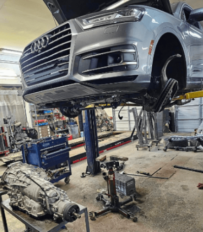 Auto repair shop with an Audi vehicle lifted for maintenance or repair. Skilled technicians working.