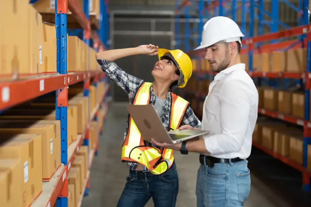 Warehouse safety inspection with two workers wearing helmets and safety vests.