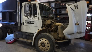 Heavy-duty truck with open hood at auto repair shop.