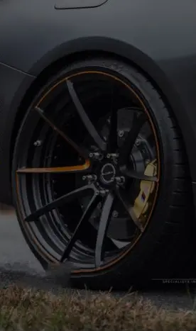 Close-up of a sleek black car wheel with orange accents and alloy rim design.