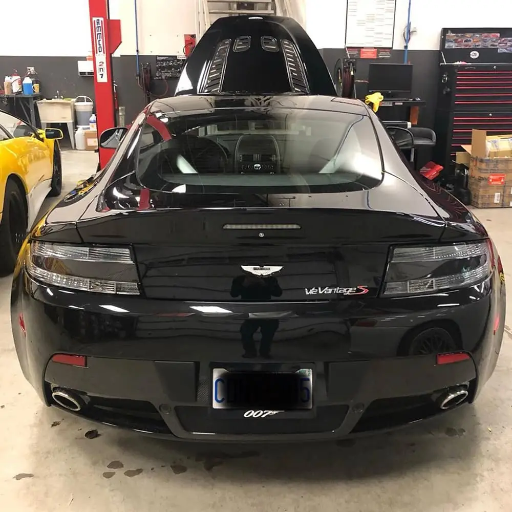 Black Aston Martin V8 Vantage S in a garage with other cars.