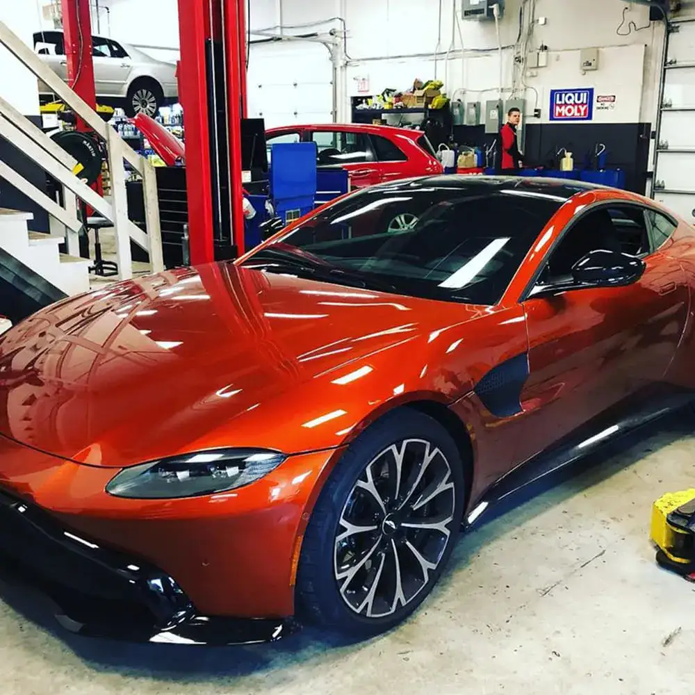 Red and black European sports car inside automotive workshop with tools and equipment.
