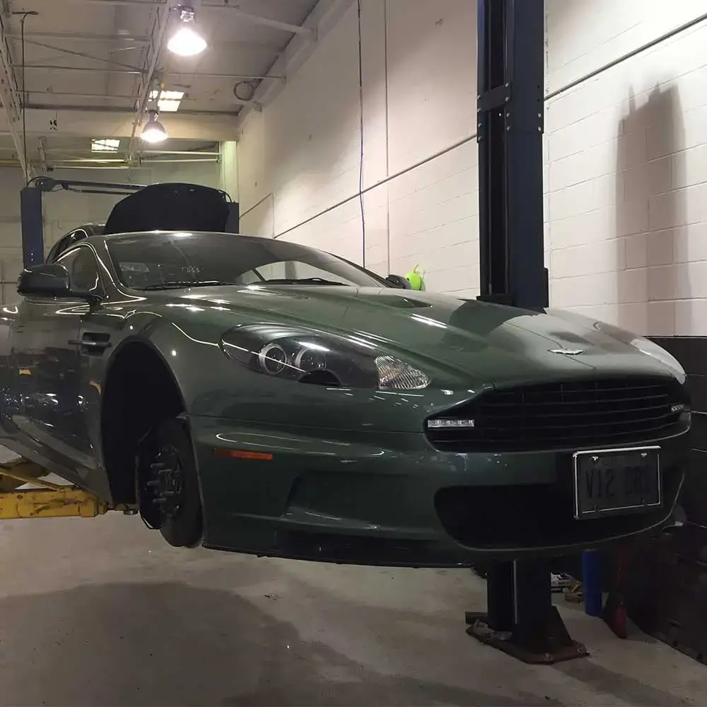 Green classic car on lift in automotive workshop with tools and equipment.
