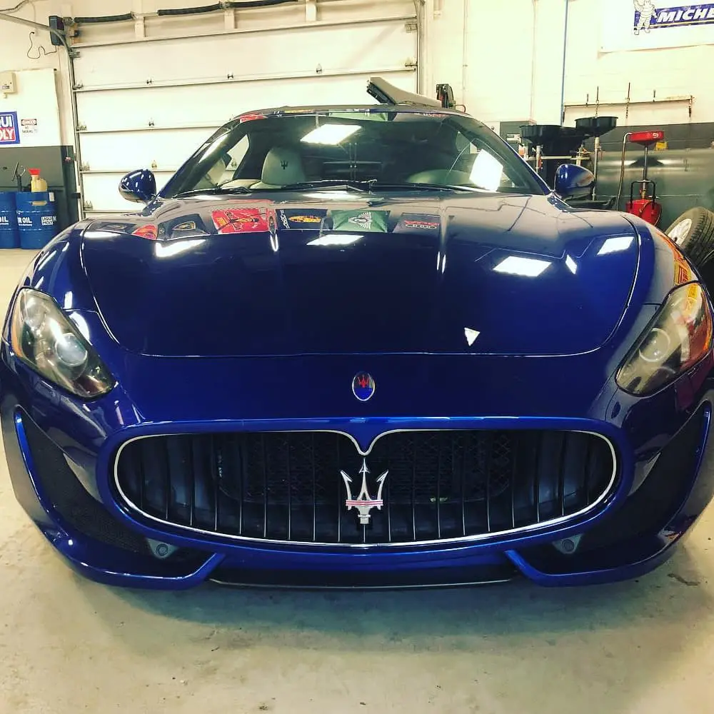 Blue Maserati sports car in garage with workshop tools.