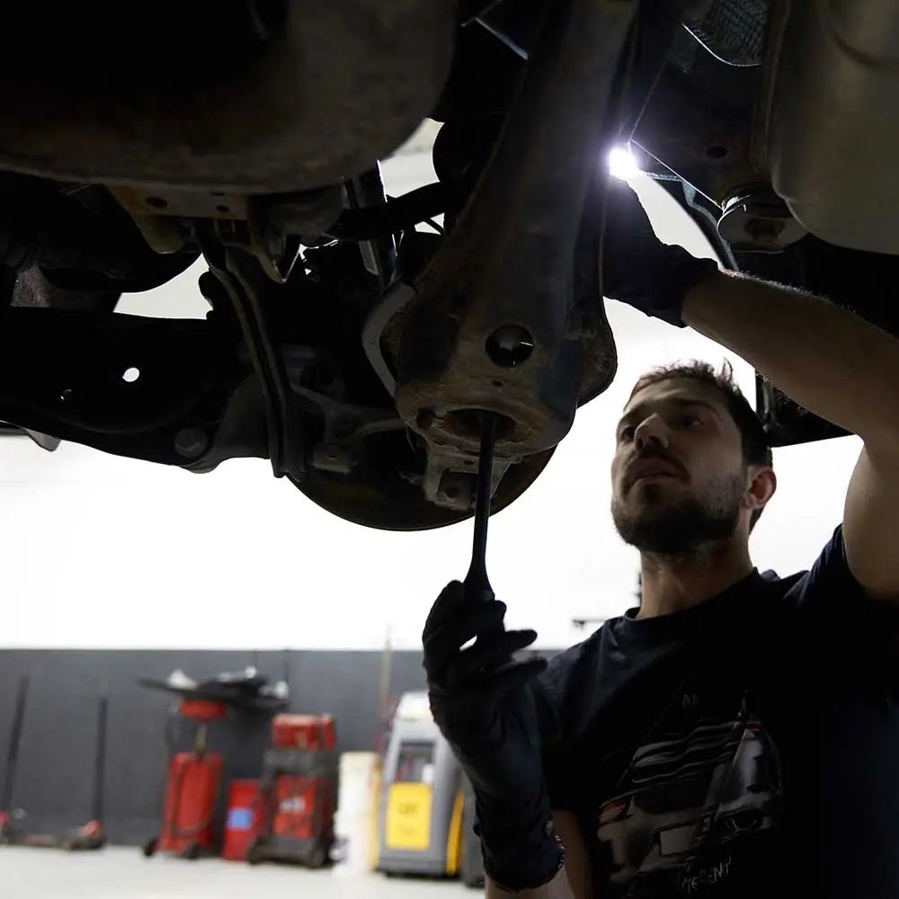 Automotive technician inspecting car underbody in workshop.