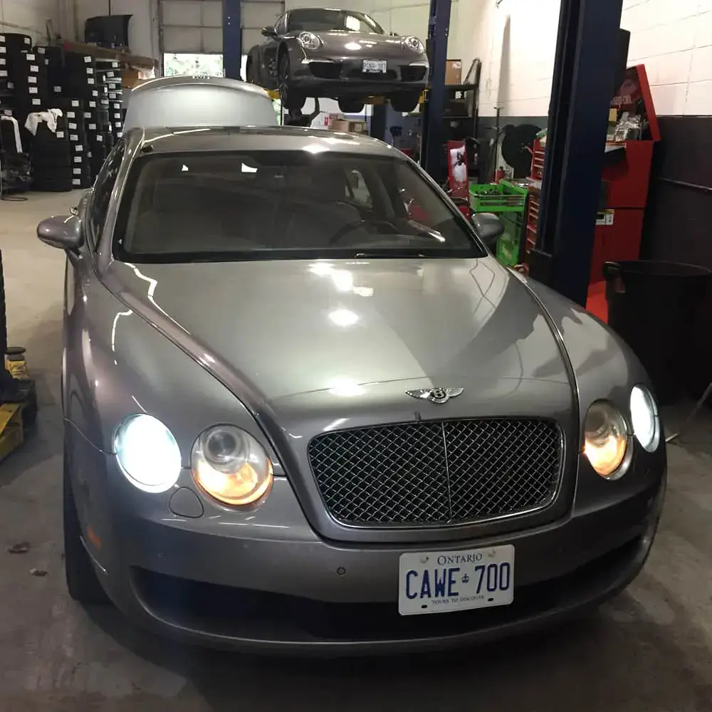 Silver Bentley luxury car in an automotive repair shop with equipment and tools.