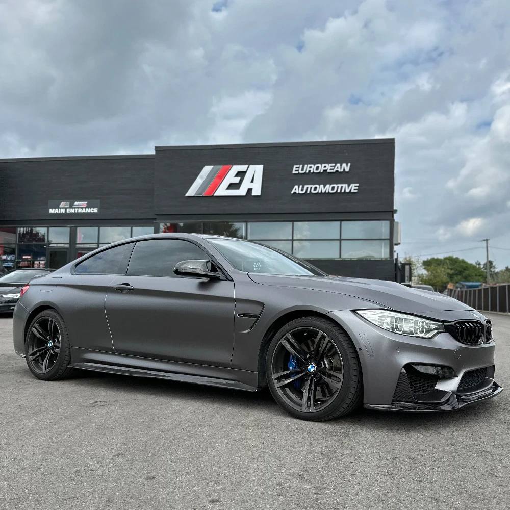 Gray BMW M4 coupe parked outside European Automotive dealership.