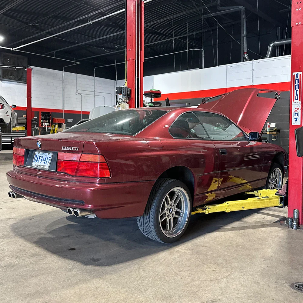 Red BMW 850Ci in auto repair shop with open hood and lift.