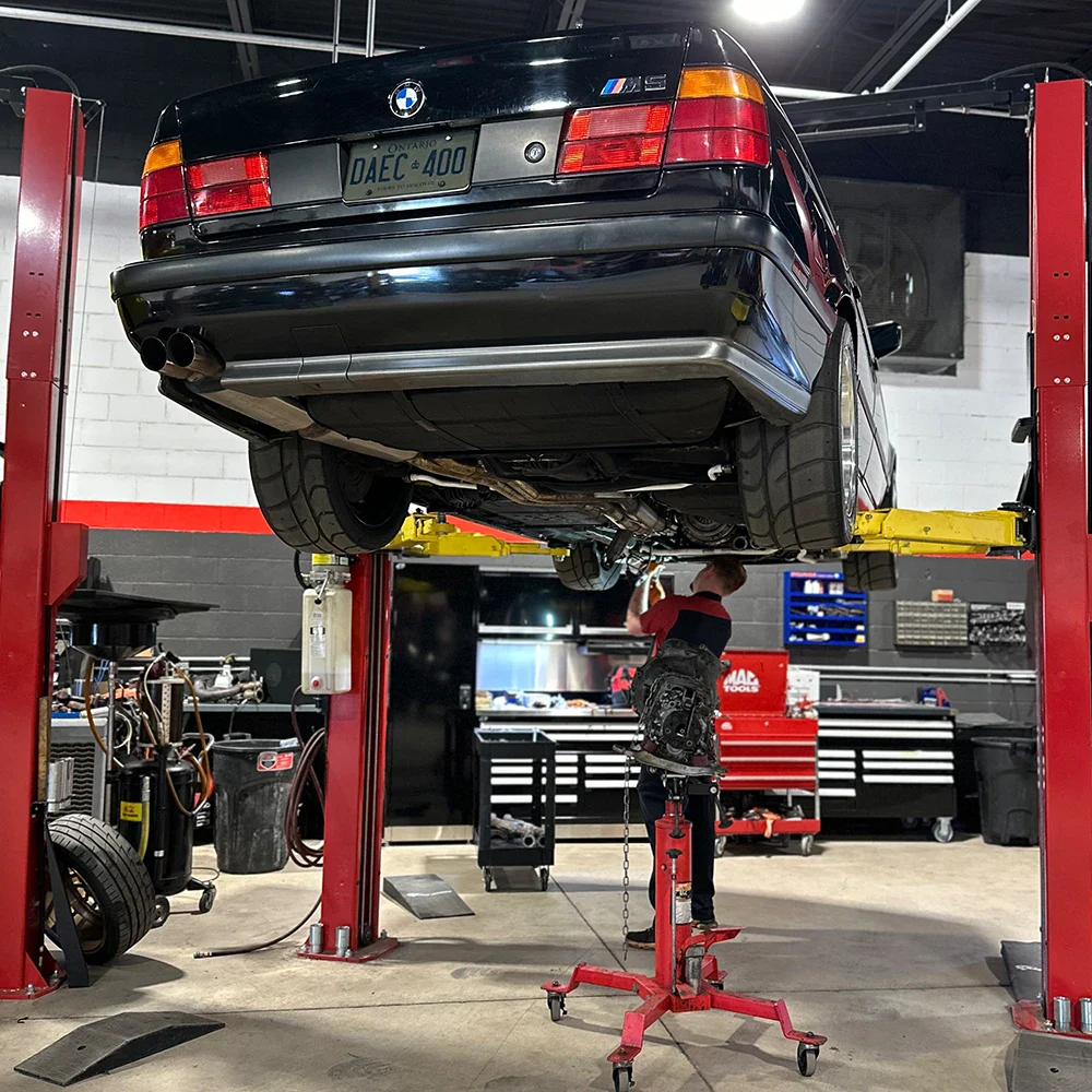 Black BMW M3 lifted on hydraulic lift in automotive repair shop.